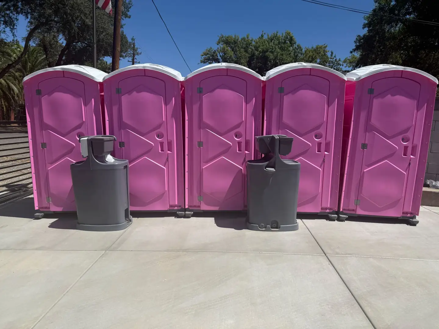 Two gray freestanding handwashing stations in front of a row of pink portable toilets