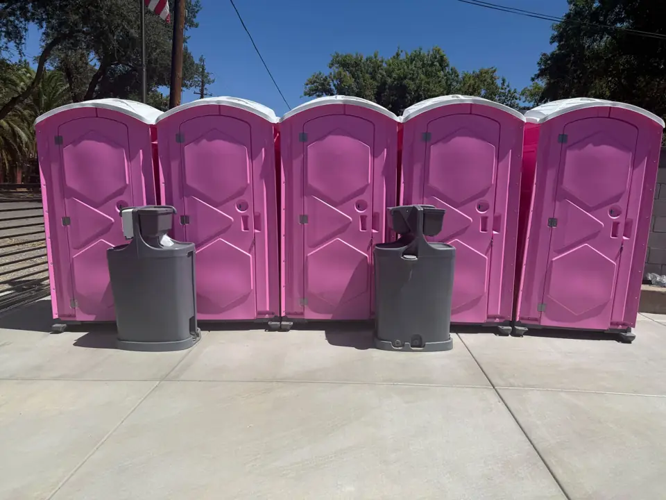 Pink portable toilets with handwashing stations set up for an event