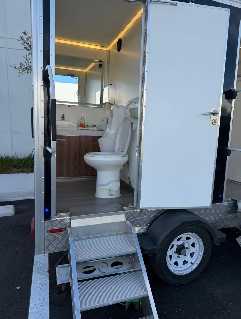 Open door of a luxury restroom trailer showing toilet and wood vanity