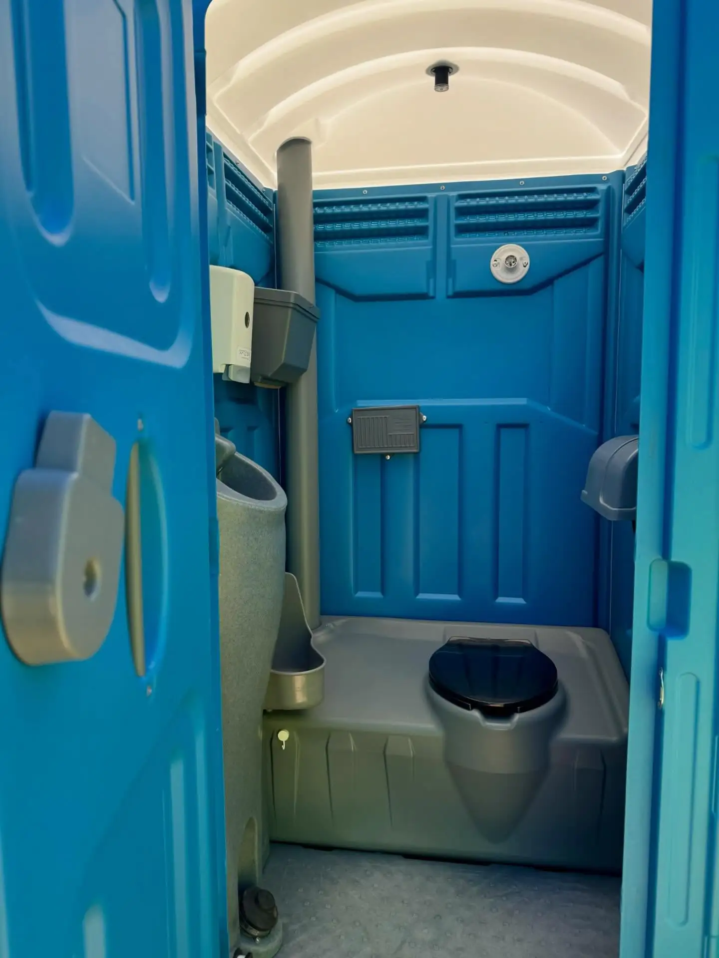 Inside a blue portable toilet showing the hand sanitizer dispenser and toilet