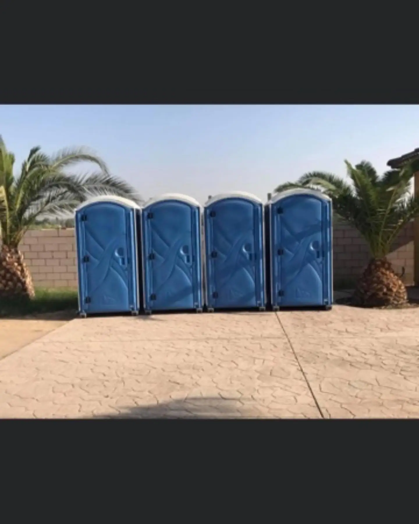 Four blue single-stall portable toilets lined up on a paved lot