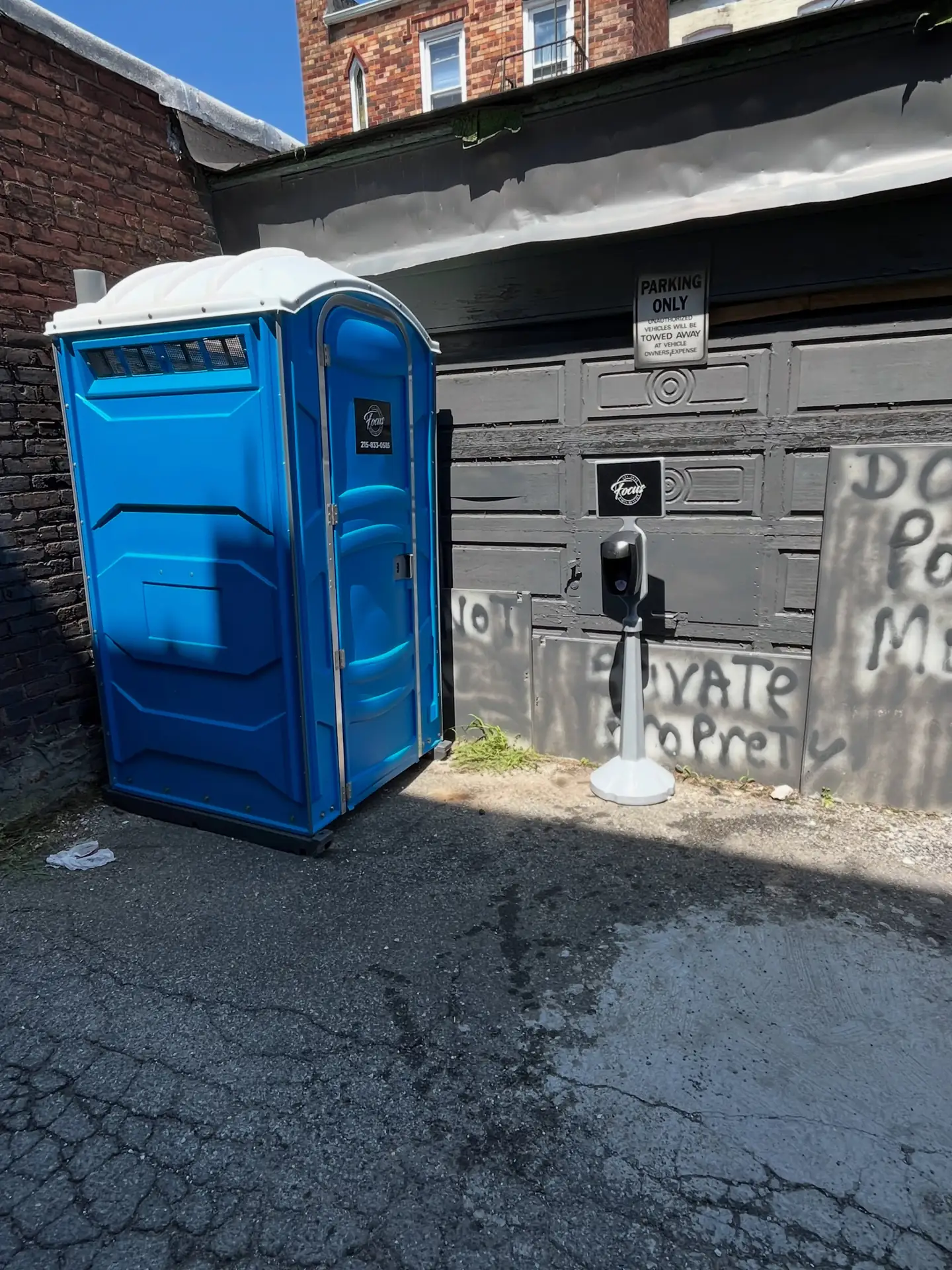 A blue porta potty placed beside a garage on an alley driveway