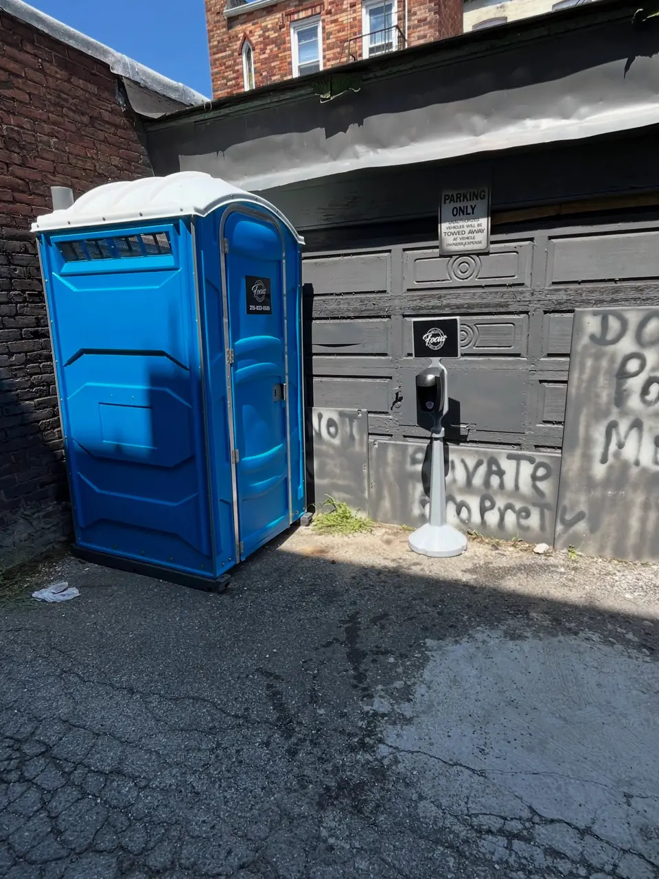 A blue porta potty placed beside a garage on an alley driveway
