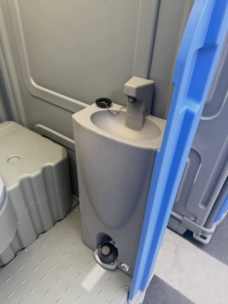 Molded gray sink with foot pump and soap dispenser inside a deluxe portable toilet