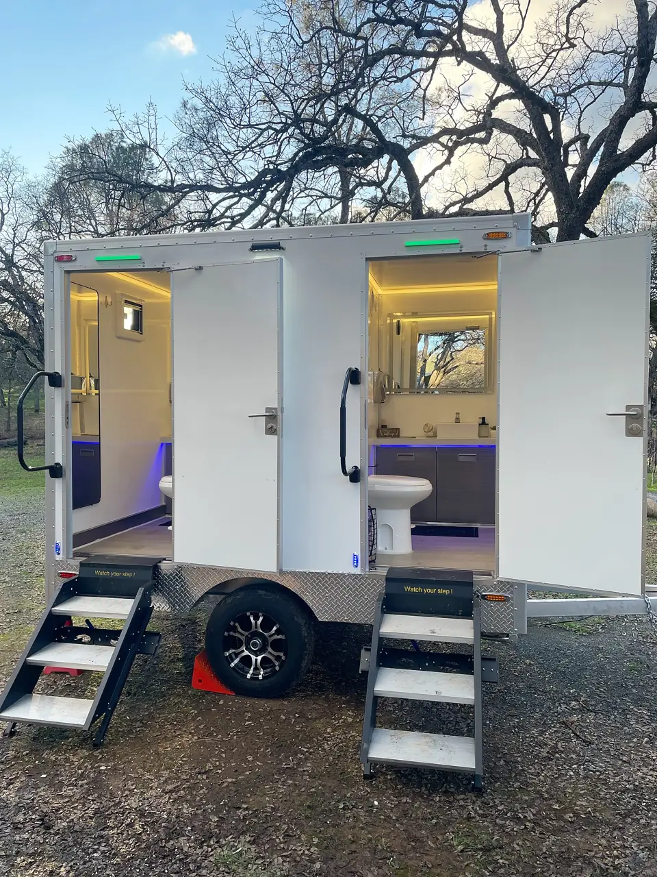 A restroom trailer lit at dusk for a summer event