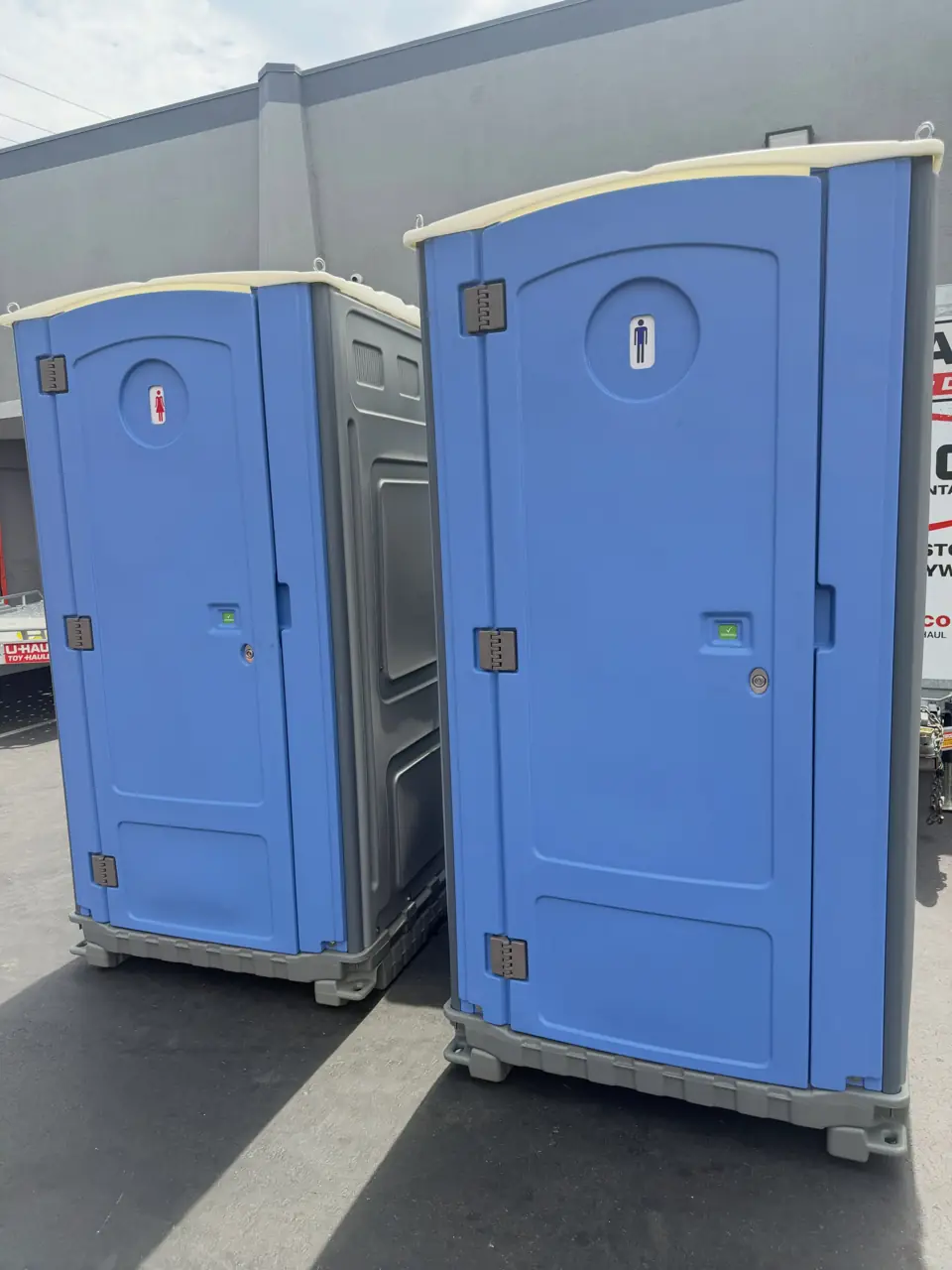 Two blue standard portable toilets on a paved lot