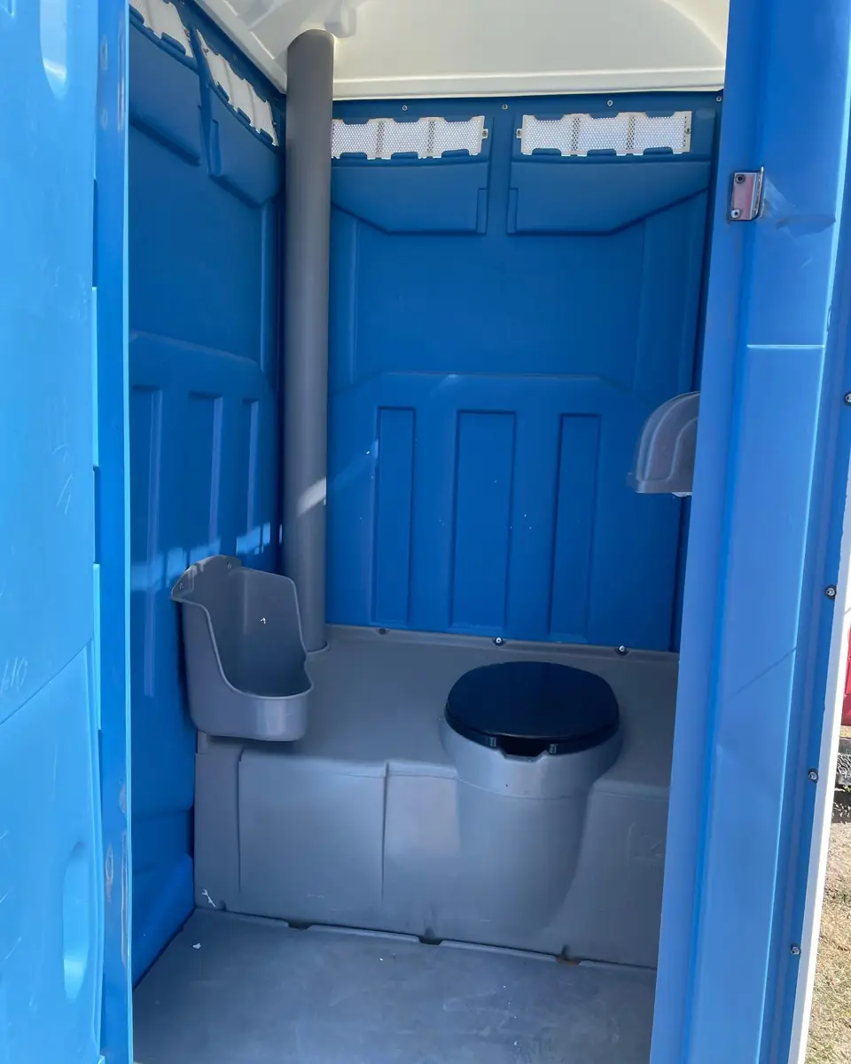 Inside a blue standard porta potty: urinal on the left wall, toilet seat and vent pipe